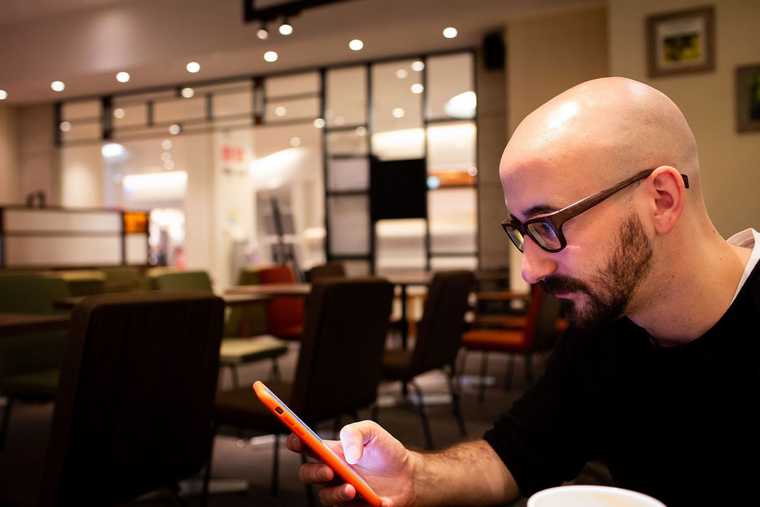 A photograph of Bryan McDowall using his phone in a cafe