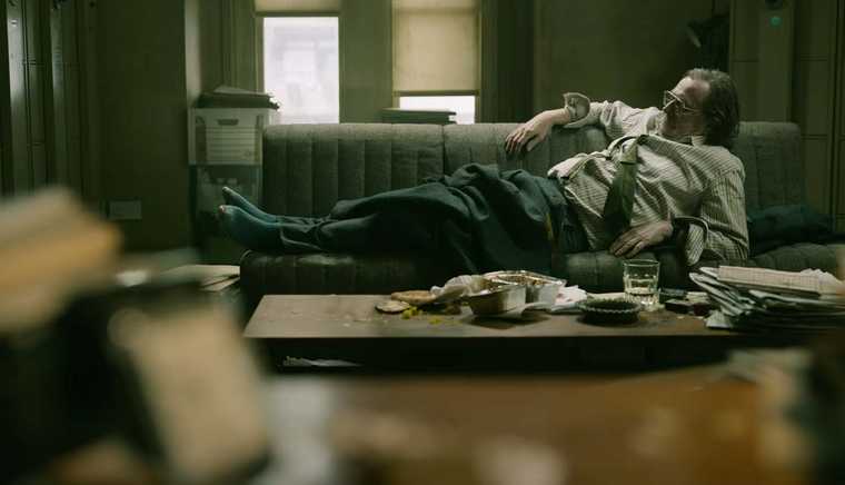 "Screen from Slow Horses TV show. Gary Oldman as Jackson Lamb, reclined on a sofa. The room is littered with food containers and paperwork."
