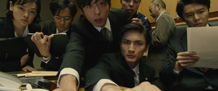 Suited Japanese staff members huddle together, facing the camera