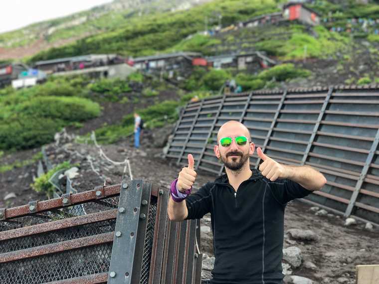A young man, posing with two thumbs up, outside the 7th station on Mt Fuji, in August.