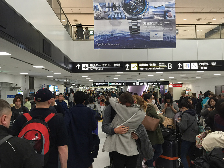 A public space in the airport filled with many people, some reuniting.