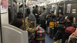 A Japanese train carriage with many people and suitcases. Most of the passengers are using their mobile devices.