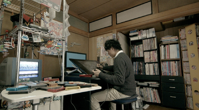 Young man sitting at a large tablet device. Gaming paraphernalia is scattered around his room.