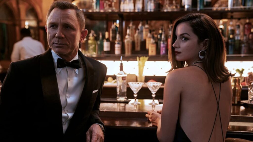 Screen from James Bond: No Time To Die, featuring Bond (Daniel Craig) in a Tuxedo and Paloma (Ana de Armas) in a cocktail dress.