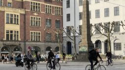 Photo from Copenhagen. People passing a monument on bicycles.