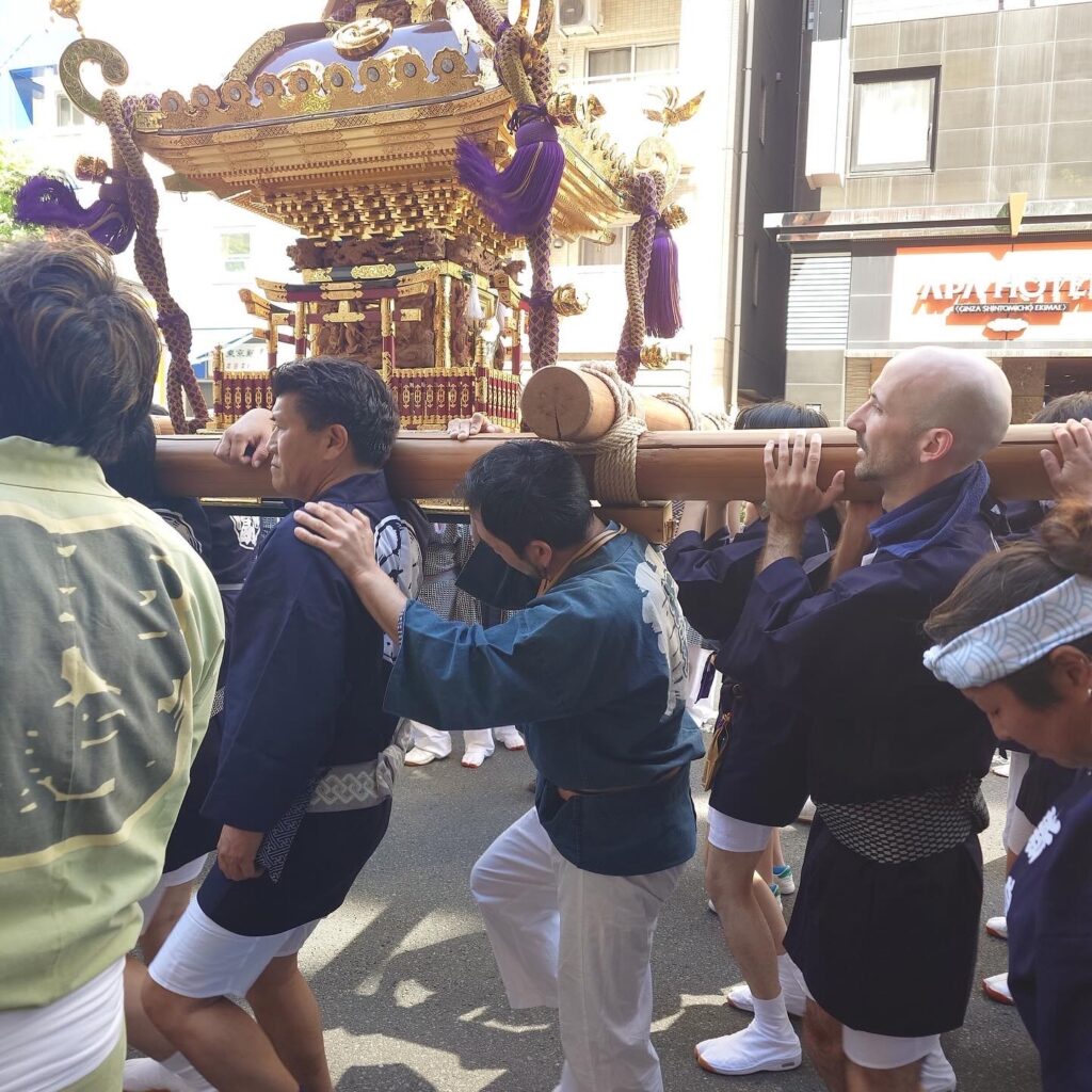 A small crowd of people lifting the mikoshi during matsuri. Wearing traditional Japanese clothing.