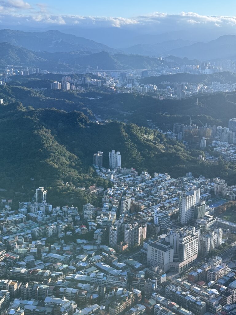 Looking over Taipei city from above. Various buildings scattered over green mountains.