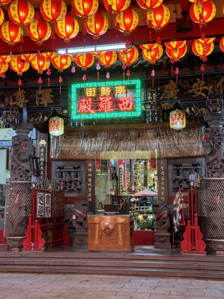 A temple in Tainan, various lanterns hang from the ceiling, and a neon sign hangs above the entrance.