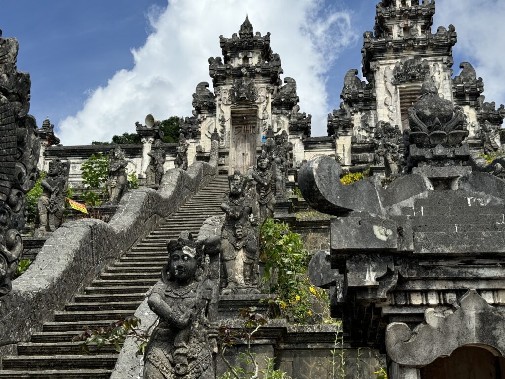 The front entrance of Lempuyang Temple in Bali. Looking up the stairs towards a decorative stone wall structure and wooden door.