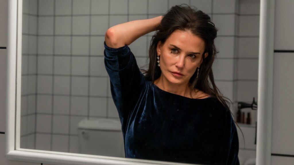 Screen from The Substance. Demi Moore holding her hair back whilst staring into the bathroom mirror.