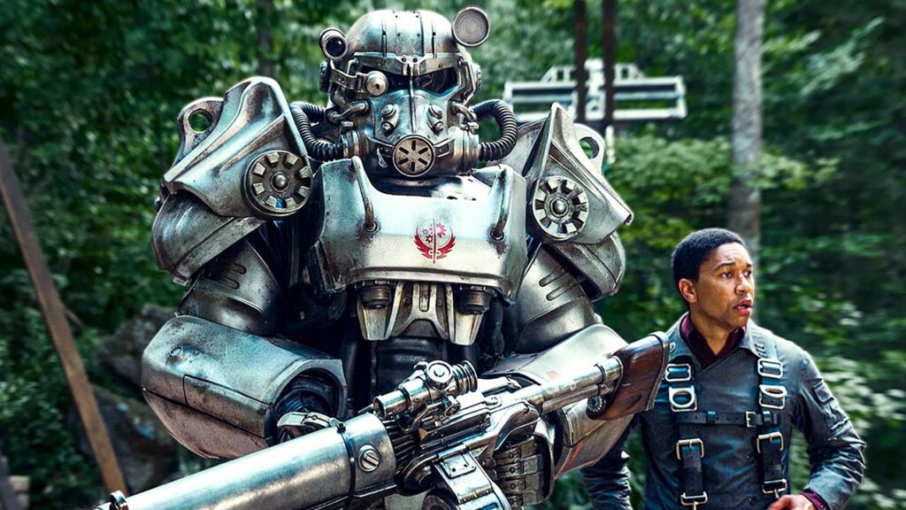 Screen from Fallout tv series. A young man standing next to a large suit of "power armour".