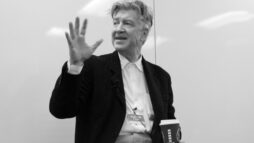 David Lynch in black and white raising his hand to emphasise his words.